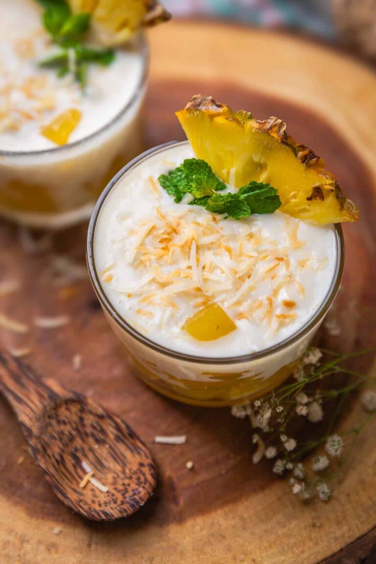 coconut pudding with pineapple jelly garnished with toasted coconut flakes, pineapple slice and mint leaves and served in shot glasses