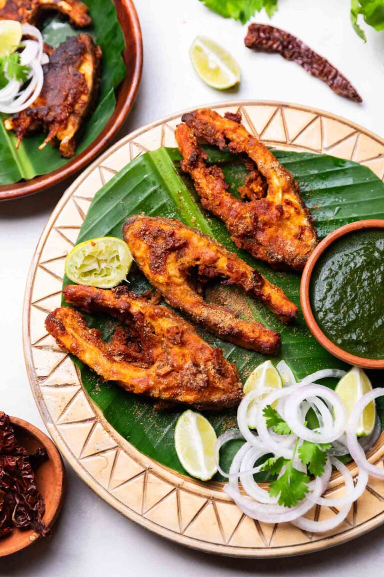 Amritsari fish fry served on a leaf platter with green chutney, onion slices, and lemon wedges