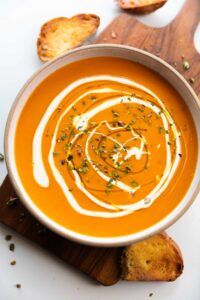 an image of roasted pumpkin pepper soup garnished with cream and rosemary along with buttered crusty bread