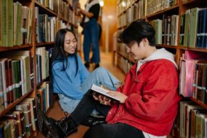 Two students reading in a library corridor.